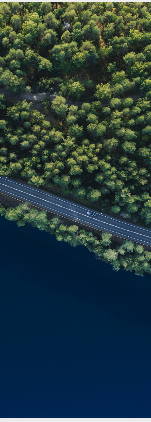 Aerial view of road with green woods by blue lakes water in summer Finland.
